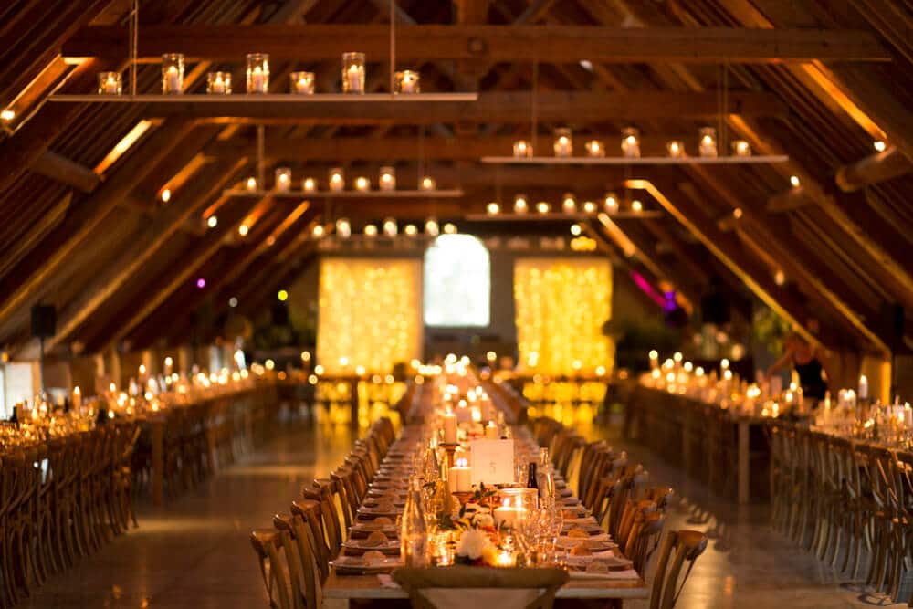 Une magnifique salle de réception pour un mariage de luxe, avec de longues tables élégamment dressées, illuminées par des bougies scintillantes. Ce cadre romantique, situé dans un domaine privé en Provence, évoque une célébration grandiose et sur mesure. L'atmosphère sophistiquée est accentuée par des éléments de décoration raffinés, parfaits pour un événement unique. By Mademoiselle C excelle dans l'organisation de mariages d'exception, offrant des lieux