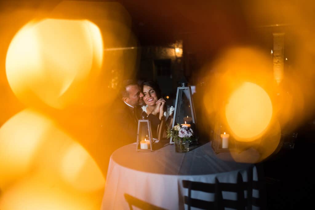 Une scène romantique d'un couple heureux lors d'une célébration de mariage dans un cadre élégant, illustrant l'expertise de By Mademoiselle C en tant que wedding planner en Provence, Côte d'Azur et Corse. La lumière douce des lanternes et des bougies crée une atmosphère intime et chaleureuse, parfaite pour un grand événement. Ce moment témoigne d'un mariage de luxe, où chaque détail est organisé sur mesure pour une expérience unique. Le décor raffiné et les