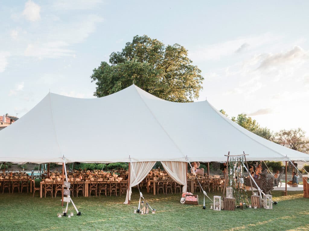 Tente élégante installée dans un jardin luxuriant pour un mariage romantique en Provence, mettant en avant une célébration grandiose. La disposition sur mesure des tables en bois et la décoration raffinée créent une atmosphère sophistiquée, idéale pour une cérémonie de luxe. Ce cadre exceptionnel, entouré de verdure, est parfait pour un événement unique, offrant une expérience de mariage sur mesure dans un domaine privé. 'By Mademoiselle C' excelle dans l'organisation de