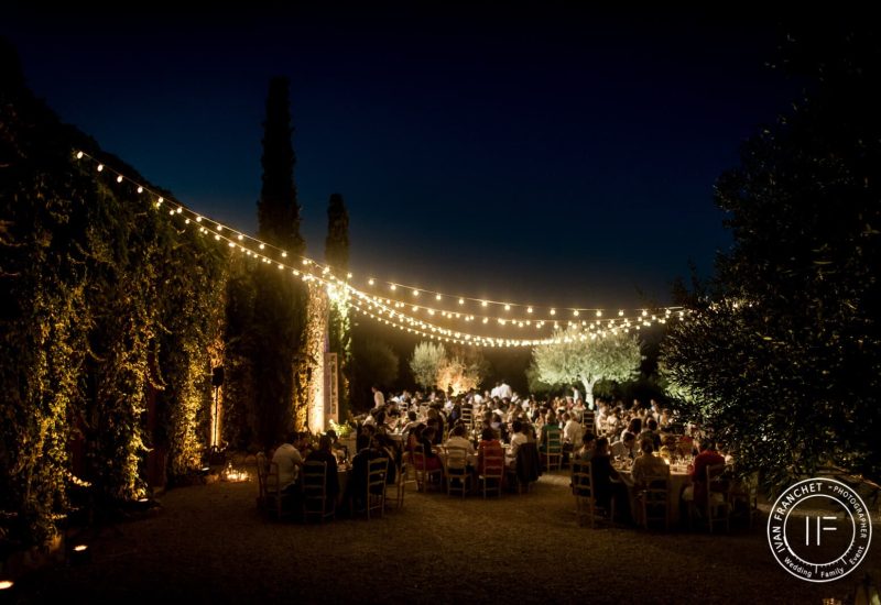 A romantic open-air dinner on a private estate, illuminated by string lights, creating an elegant ambience for a grand celebration. This evening, organized by By Mademoiselle C, embodies the essence of a luxury wedding in Provence, French Riviera &amp; Corsica. Guests enjoy a unique setting, surrounded by lush gardens, for a tailor-made event. This grand event is the reflection of an organization.