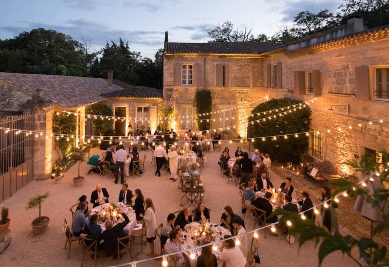 Un élégant dîner en plein air organisé par 'By Mademoiselle C', wedding planner en Provence, Côte d'Azur & Corsica, mettant en scène une célébration grandiose sous des guirlandes lumineuses. Cette soirée romantique, au cœur d'un domaine privé, offre un cadre sophistiqué pour un mariage sur mesure. Les invités profitent d'une ambiance chaleureuse et intimiste, parfaite pour une cérémonie unique. Les magnifiques murs en pierre et la verdure environnante ajout