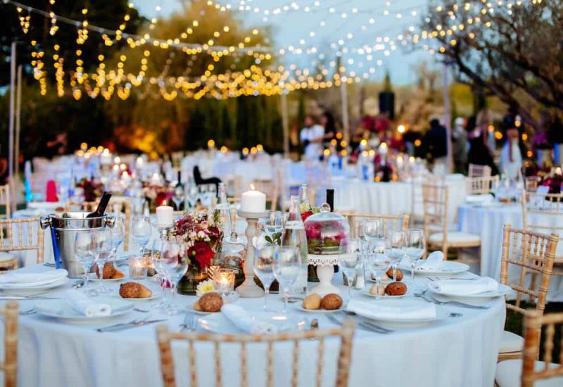 An elegantly set table for a grand event, in the heart of a romantic garden under a starry sky. Strings of lights create a warm, sophisticated atmosphere, perfect for a luxury wedding celebration. Every detail, from the delicate flowers to the crystal glasses, reflects By Mademoiselle C's expertise in organizing made-to-measure weddings in Provence, the French Riviera and Corsica.