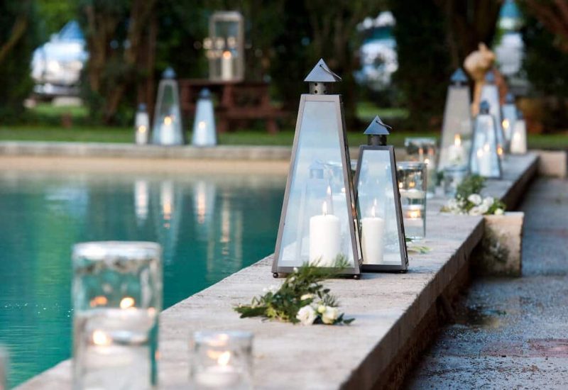 Romantic poolside lighting on a private estate, creating an elegant atmosphere for a luxury wedding in Provence. Twinkling lanterns and candles add a sophisticated touch to this bespoke celebration, ideal for a grand ceremony. This enchanting setting, surrounded by greenery, is perfect for a unique and memorable event, making every moment a dream come true. By Mademoiselle C transforme des lieux