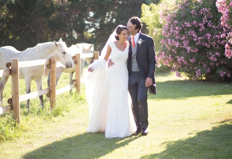 An elegant couple stroll through an enchanting garden, surrounded by white horses and colorful flowers, illustrating the magic of a romantic wedding. This scene evokes a grand celebration, perfectly orchestrated by 'By Mademoiselle C', the luxury wedding planner in Provence, French Riviera and Corsica. With an idyllic natural setting and meticulous attention to detail, every moment of this dream wedding becomes a unique experience.