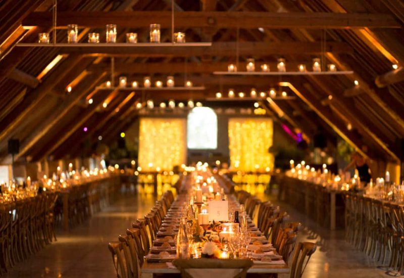 A magnificent reception hall for a luxury wedding, with long, elegantly laid tables illuminated by sparkling candles. This romantic setting, situated on a private estate in Provence, evokes a grandiose, tailor-made celebration. The sophisticated atmosphere is accentuated by refined decorative elements, perfect for a unique event. By Mademoiselle C excels in the organization of exceptional weddings, offering venues