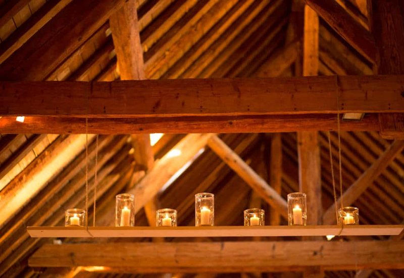 Elegant glass lighting illuminates a magnificent wooden reception room, ideal for a romantic wedding in Provence. This sophisticated setting, with its exposed beams, creates an intimate atmosphere for a grand ceremony. By Mademoiselle C's bespoke organization of this unique event guarantees a luxurious celebration, showcasing exceptional venues for a dream come true. Perfect for a grand ceremony on a private estate, this space evokes the elegance of the past.