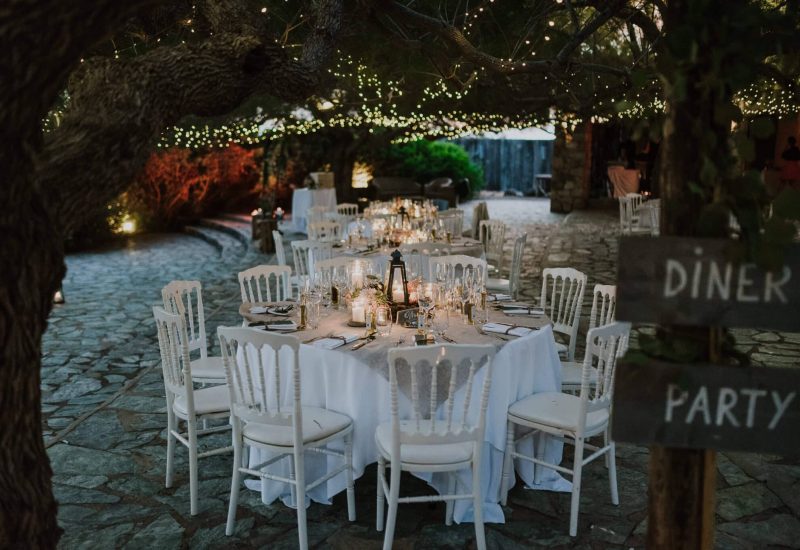An elegant al fresco dinner setting, showcasing the expertise of 'By Mademoiselle C' as Wedding Planner in Provence, French Riviera &amp; Corsica. Beautifully laid tables, under a sparkling starry sky, create a romantic atmosphere for a grand celebration. This exceptional setting, surrounded by greenery, evokes a tailor-made wedding, where every detail is carefully orchestrated.