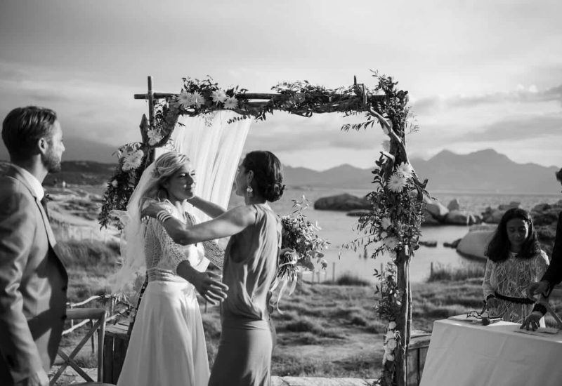 A romantic celebration of a luxury seaside wedding, featuring an open-air ceremony in a breathtaking natural setting. The flower-decorated arch and mountain backdrop underline the elegance and sophistication of this bespoke event. By Mademoiselle C, wedding planner in Provence, French Riviera and Corsica, creates unique and memorable celebrations, transforming every moment into an unforgettable experience.