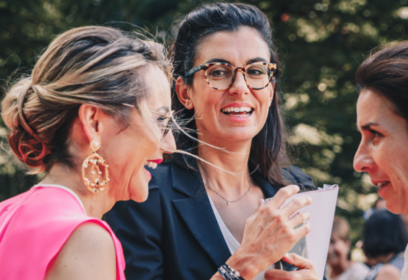 An elegant wedding planner chats with guests at a romantic ceremony in Provence, showcasing 'By Mademoiselle C''s expertise in luxury weddings. This scene captures the sophisticated atmosphere of a bespoke event, ideal for a grand celebration on a private estate. Laughter and smiles evoke the ambiance of a dream wedding, surrounded by the natural beauty of the Côte d'Azur.