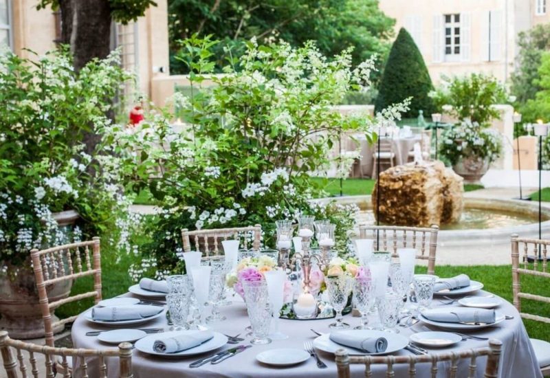 Elegantly set table in a lush garden, surrounded by white flowers and verdant trees, illustrating a romantic and sophisticated ceremony. Perfect for a luxury wedding, this reception space on a private estate in Provence evokes a grand celebration. Every detail is carefully designed to create a bespoke event, offering an exceptional setting for a dream wedding. The peaceful atmosphere and elegance of the venue make