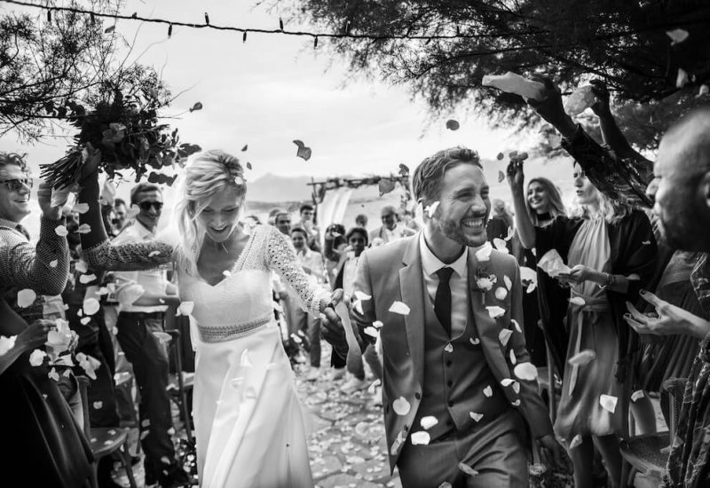 Célébration romantique d'un mariage de luxe en Provence, avec un couple rayonnant sous une pluie de pétales, entouré d'amis et de famille. Ce moment capturé illustre l'expertise de By Mademoiselle C dans l'organisation de cérémonies sur mesure dans des lieux exceptionnels. L'atmosphère élégante et sophistiquée de cet événement fait de chaque mariage un moment unique, parfait pour une grande célébration au cœur de la Côte d'