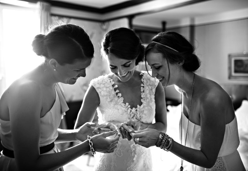 An intimate and joyful moment before a luxury wedding, with the bride surrounded by her friends, each smiling and elegant. This bespoke wedding, organized by By Mademoiselle C, promises a grandiose ceremony in Provence, the French Riviera and Corsica. The romantic and sophisticated atmosphere is enhanced by refined details, reflecting the brand's expertise in creating unique and memorable events.