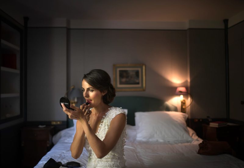 An elegant bride prepares in a refined room, embodying the luxury of a bespoke wedding in Provence, the French Riviera and Corsica. The romantic, sophisticated atmosphere evokes a grand celebration, perfect for a unique event. The delicate details of her dress highlight the craftsmanship of a grand wedding, while the intimate setting of a hotel suite underscores the bespoke organization of an exceptional ceremony. This moment captured