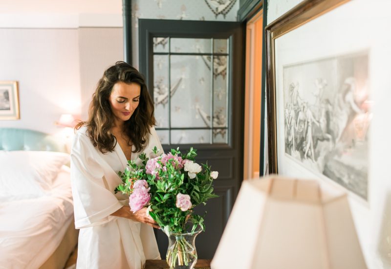 An elegant bride in a white robe arranges a bouquet of pastel flowers in a refined room, a symbol of preparation for a luxury wedding in Provence. This romantic scene evokes a sophisticated ambience, perfect for a bespoke event. By Mademoiselle C' excels in organizing grandiose celebrations in exceptional locations, combining charm and elegance, whether in a private estate or a luxury hotel. Every