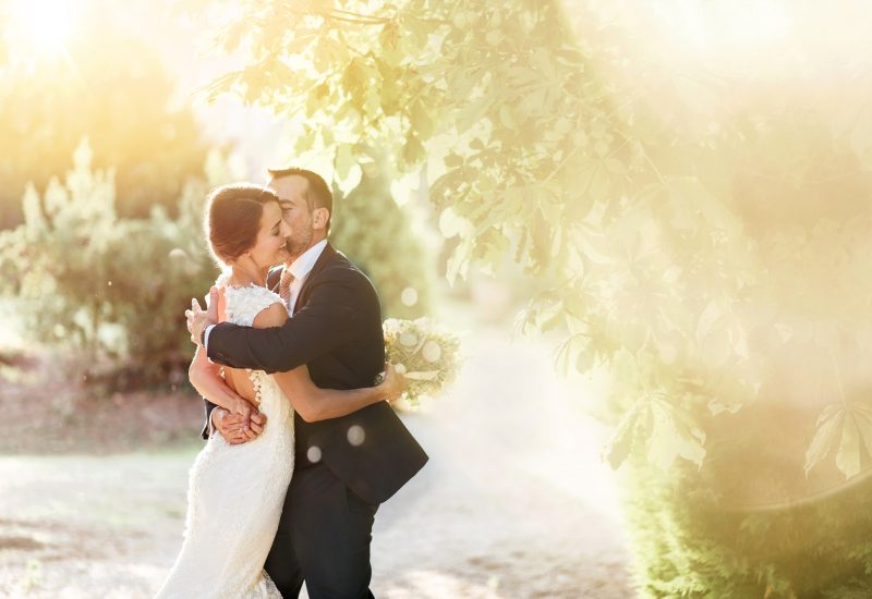 A happy couple embrace in a romantic, sunny setting, symbolizing the essence of a luxury wedding in Provence. This magical moment evokes a grandiose ceremony, where every detail is carefully organized to create a tailor-made event. Surrounded by lush greenery, they embody the dream of a unique celebration on a private estate. With an elegant and sophisticated atmosphere, 'By Mademoiselle C' transforms every