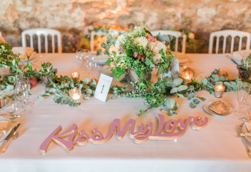 An elegantly set table for a luxury wedding in Provence, with delicate flowers and twinkling candles, creating a romantic and sophisticated atmosphere. This bespoke wedding décor enhances an exceptional event on a private estate, ideal for a grand celebration. Decorative elements, such as "Kiss My Love" signage, add a personal touch to this wedding dream. Perfect for a couple looking to organize a