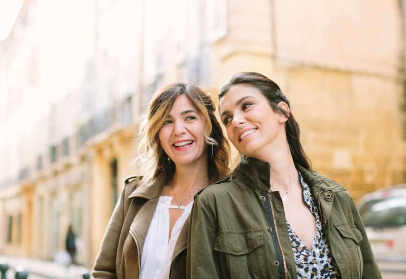 Deux femmes souriantes dans une rue pittoresque, illustrant l'esprit de 'By Mademoiselle C', wedding planner en Provence, Côte d'Azur et Corse. Leur élégance évoque des mariages romantiques et des célébrations grandioses. Avec une expertise dans l'organisation d'événements uniques, elles créent des cérémonies sur mesure dans des domaines privés et des lieux exceptionnels.