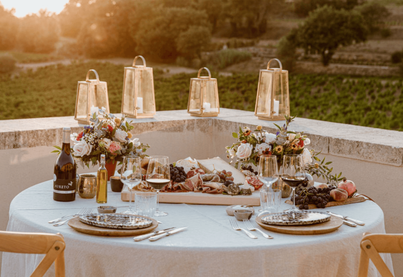 An elegantly set table for a grand wedding in Provence, surrounded by verdant vineyards, evokes a romantic and sophisticated atmosphere. This festive scene showcases a bespoke event, perfect for a luxurious celebration. Golden lanterns twinkle at sunset, adding a touch of magic to this private estate. With refined dishes and exquisite wines, this exceptional setting is ideal for a dream wedding or a unique occasion.