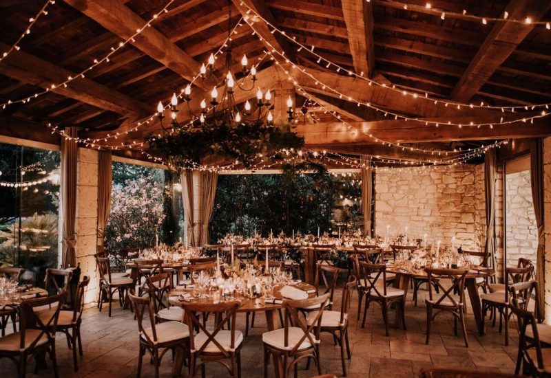 An elegant and romantic room for a luxury wedding, decorated with garlands of lights and chandeliers, offering the perfect setting for a grandiose celebration. Set in a private estate in Provence, this space evokes a sophisticated yet warm atmosphere, ideal for a tailor-made event. Carefully laid tables, surrounded by greenery, create an intimate atmosphere for an exceptional wedding. The perfect choice for a romantic wedding