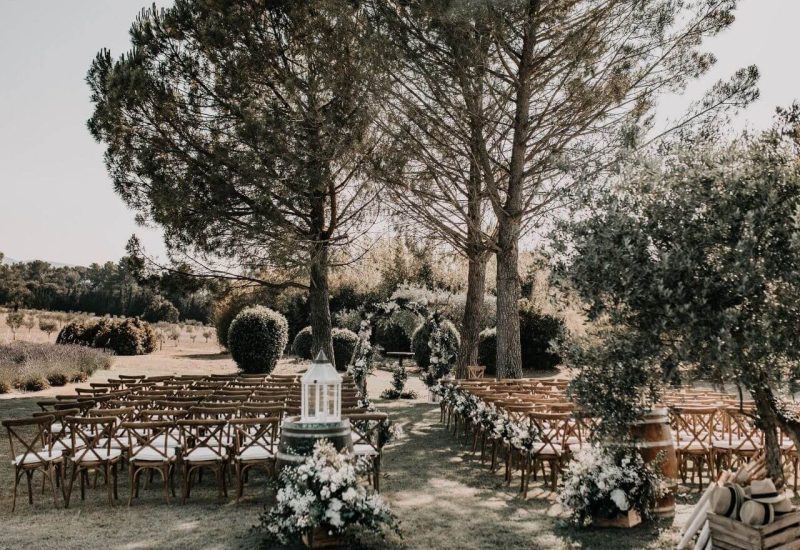 A romantic, elegant setting for a bespoke wedding ceremony, featuring wooden chairs arranged beneath majestic trees. This exceptional venue, nestled in a private estate in Provence, evokes an atmosphere of luxury and sophistication, perfect for a grand celebration. Delicate floral touches add a touch of charm to this unique event, ideal for a dream wedding in an idyllic setting. By Mademoiselle C makes every moment an unforgettable one.