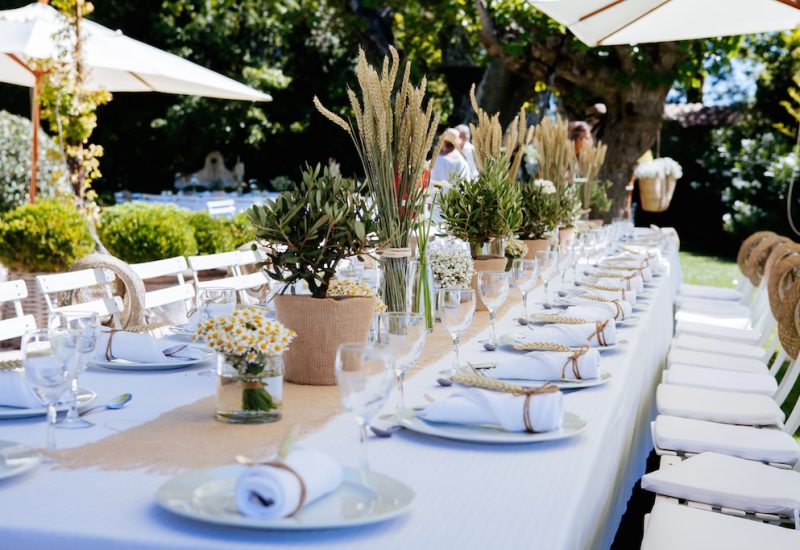 Elegantly set table for a romantic outdoor celebration, showcasing By Mademoiselle C's expertise as Wedding Planner in Provence, French Riviera &amp; Corsica. Natural elements such as green plants and delicate flowers create a sophisticated atmosphere for a grand event. The carefully thought-out layout reflects a bespoke organization, ideal for a luxury wedding or a grand ceremony on a private estate.