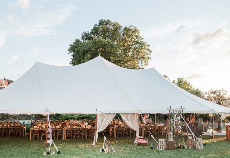 Elegant tent set in a lush garden for a romantic wedding in Provence, showcasing a grand celebration. The bespoke arrangement of wooden tables and refined decor create a sophisticated atmosphere, ideal for a luxurious ceremony. This exceptional setting, surrounded by greenery, is perfect for a unique event, offering a bespoke wedding experience in a private estate. By Mademoiselle C' excels in the organization of