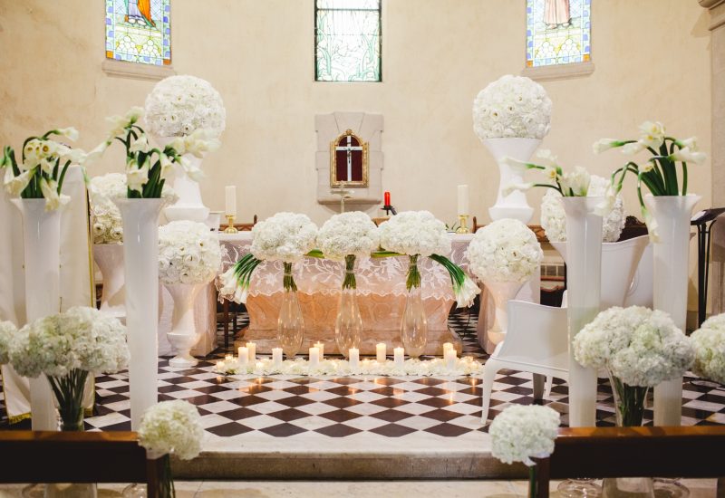 Une élégante cérémonie de mariage se déroule dans une chapelle, décorée de somptueuses fleurs blanches et de bougies, créant une atmosphère romantique et sophistiquée. En tant que Wedding Planner en Provence, Côte d'Azur & Corsica, By Mademoiselle C organise des événements de luxe sur mesure, transformant chaque moment en une célébration grandiose. Ce cadre exceptionnel, avec ses détails raffinés, illustre parfaitement une expérience de mariage unique.