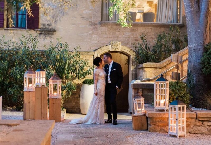 Un couple élégant se tient dans un cadre romantique, illuminé par des lanternes, dans un domaine privé en Provence. Cette scène évoque une cérémonie grandiose, parfaite pour un mariage de luxe. L'atmosphère sophistiquée et intime souligne l'expertise de 'By Mademoiselle C' en matière d'organisation de mariages sur mesure. Le jardin environnant et l'architecture raffinée créent le cadre idéal pour une célébration exceptionnelle, où chaque détail contribue à réaliser