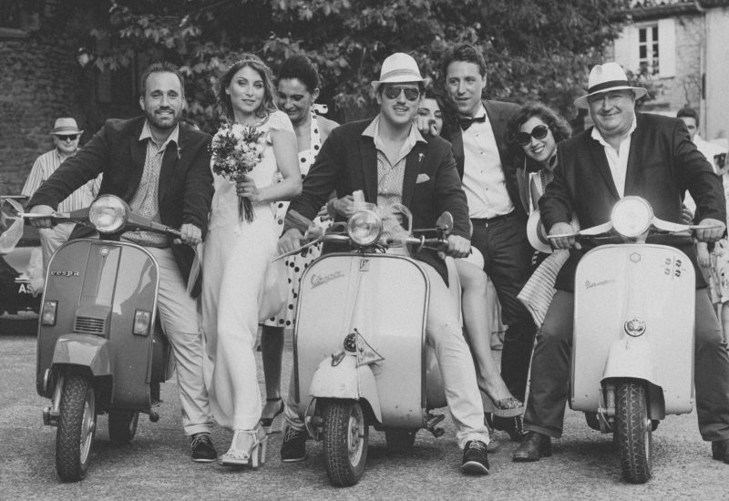 Élégante scène de mariage avec des invités joyeux sur des scooters vintage, illustrant une célébration unique et romantique. Ce moment capturé par 'By Mademoiselle C', expert en organisation de mariages de luxe en Provence, Côte d'Azur et Corse, met en avant l'atmosphère conviviale d'un grand événement. La touche personnalisée et le cadre pittoresque ajoutent une dimension magique à ce mariage sur mesure, idéal pour une grande cérémonie.