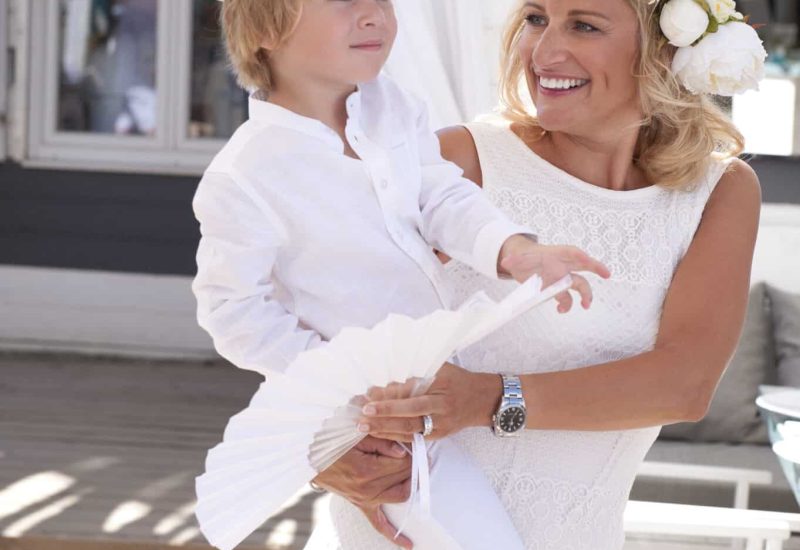 Une mère heureuse portant son enfant dans un cadre élégant et romantique, parfait pour un mariage de luxe en Provence, Côte d'Azur et Corse. Cette scène capture l'essence d'un événement sur mesure, où chaque détail est pensé pour créer une célébration grandiose. L'atmosphère dégage une sophistication unique, idéale pour un mariage de rêve ou une cérémonie exceptionnelle. Les vêtements blancs évoquent la pureté d'un mariage romantique, tandis que le décor environnant évoque un domaine