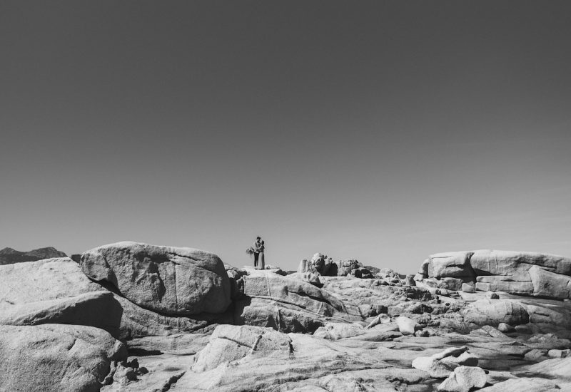 Un couple se tenant sur des rochers majestueux, symbolisant une cérémonie romantique unique, idéale pour un mariage de luxe en Corse. L'atmosphère élégante et sophistiquée évoque un grand célébration, tandis que le paysage naturel et sauvage souligne l'importance de choisir des lieux d'exception pour des événements sur mesure. Ce cadre spectaculaire est parfait pour un rêve de mariage, où chaque détail est soigneusement orchestré par By Mademoiselle C, spécialiste des mariages