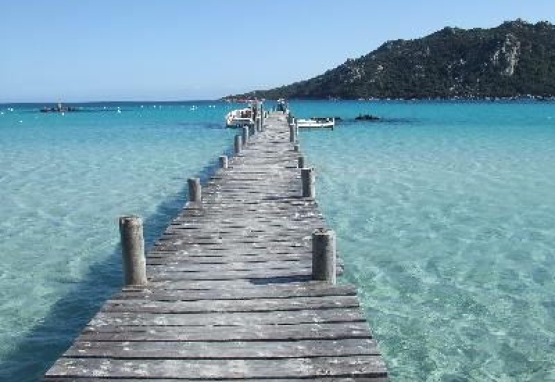 Wooden bridge leading to turquoise waters, symbolizing an idyllic setting for a luxury wedding in Corsica. This exceptional venue offers a romantic and elegant atmosphere, perfect for a grand ceremony. With breathtaking sea views, it's ideal for a bespoke celebration, creating a unique event. By Mademoiselle C' excels in organizing weddings on this magnificent island, guaranteeing unforgettable memories.