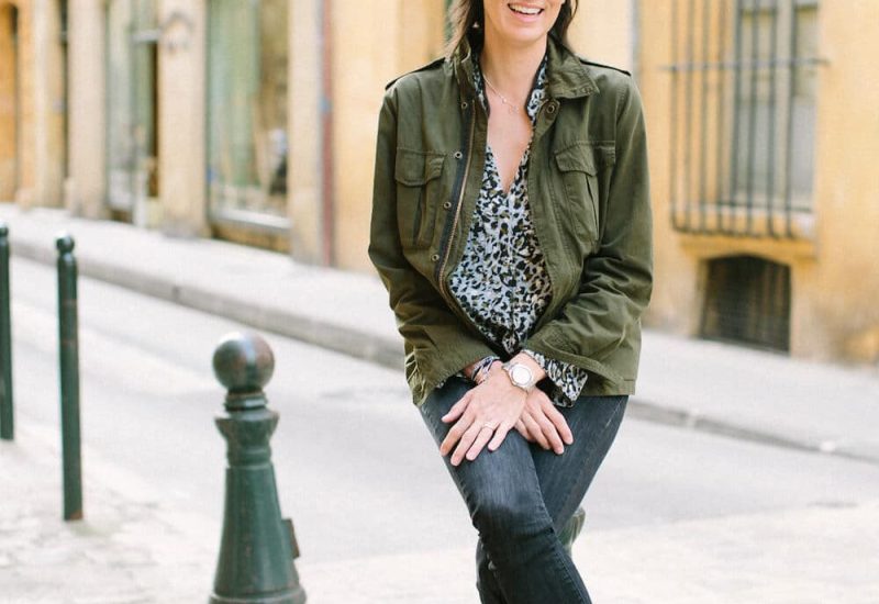 An elegant wedding planner smiling on a picturesque street, embodying the style of 'By Mademoiselle C', specialist in luxury weddings in Provence, the French Riviera and Corsica. Her expertise in organizing tailor-made ceremonies is highlighted, promising unique events in exceptional locations. The romantic, sophisticated atmosphere evokes grandiose celebrations on private estates, in lush gardens or in the heart of the French Riviera.