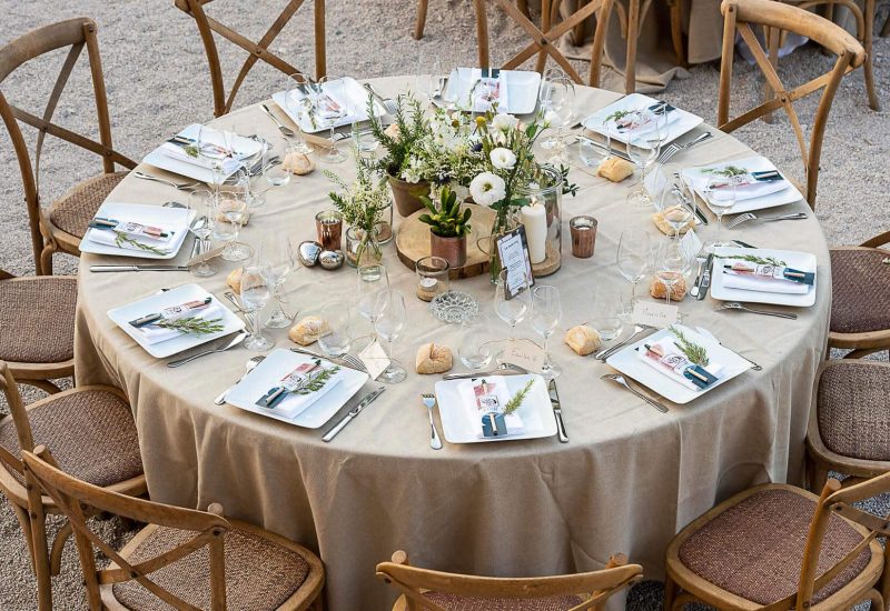 An elegantly set table for a romantic wedding ceremony, featuring the expertise of By Mademoiselle C, wedding planner in Provence, French Riviera &amp; Corsica. This intimate, sophisticated setting perfectly illustrates a bespoke event, with refined décor elements and personalized details. Surrounded by picturesque scenery, this grand celebration promises an unforgettable experience for a luxury wedding, in an exceptional private estate. A