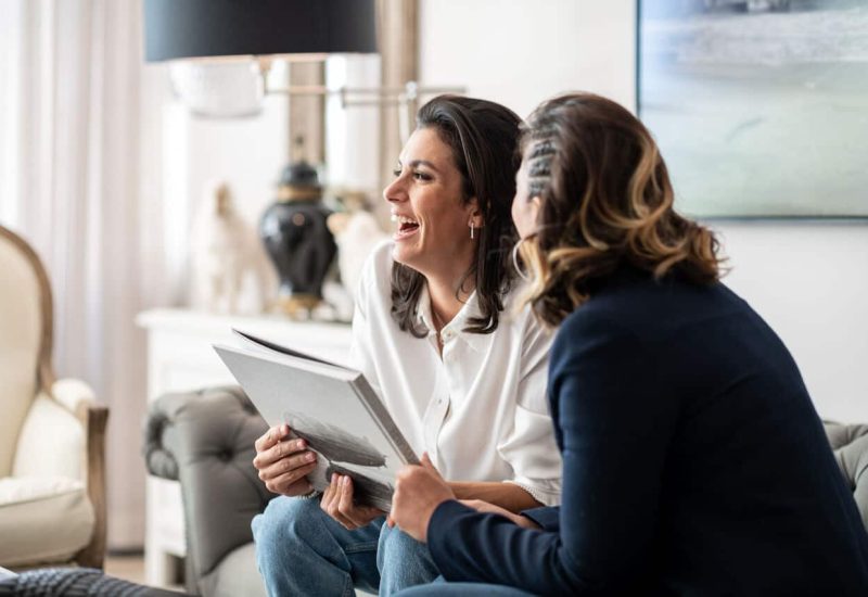 Two smiling women discuss a wedding project in an elegant setting, showcasing the expertise of By Mademoiselle C, wedding planner in Provence, the French Riviera and Corsica. The romantic, sophisticated atmosphere of this exchange evokes the creation of a grand ceremony in a private estate. With a tailor-made approach, they envision a luxury wedding, carefully designed to offer a unique experience.