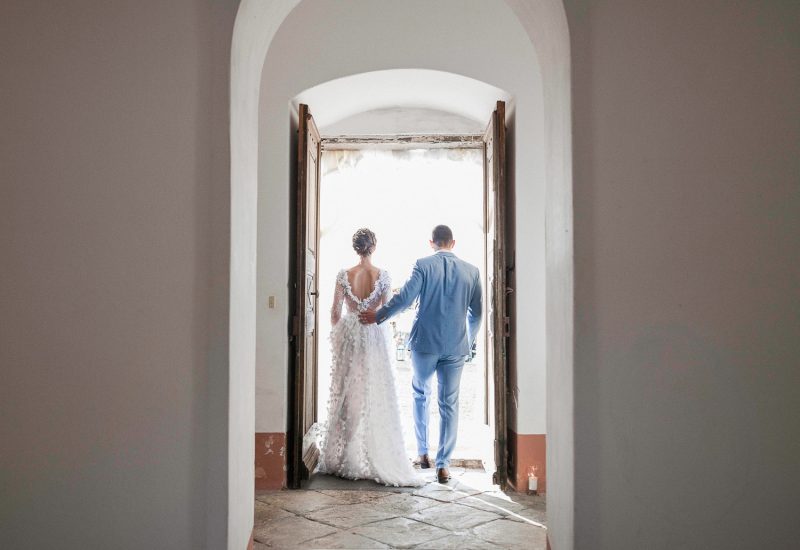 Un couple se tenant par la main, sortant d'une élégante demeure, symbolisant un moment romantique et intime, parfait pour un mariage de luxe en Provence, Côte d'Azur et Corse. Cette scène évoque une organisation sur mesure d'une cérémonie grandiose dans un domaine privé, où chaque détail est pensé pour créer un événement unique. L'atmosphère raffinée et sophistiquée de cet endroit sublime souligne l'expertise de 'By Mademoiselle C' dans la création