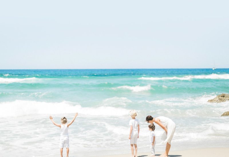 Une mère et ses enfants s'émerveillent sur une plage ensoleillée de la Côte d'Azur, symbolisant l'atmosphère romantique et élégante des événements organisés par By Mademoiselle C. Cette scène évoque des souvenirs de célébrations de luxe et de mariages sur mesure dans des lieux exceptionnels. L'environnement côtier, avec ses vagues scintillantes et son ciel azur, rappelle le cadre parfait pour une cérémonie grandiose ou une célébration
