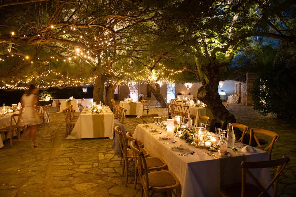 Un cadre romantique et élégant pour une célébration de mariage de luxe en Provence, Côte d'Azur et Corse, mettant en avant une organisation sur mesure par By Mademoiselle C. Les tables soigneusement dressées sous les arbres illuminés créent une atmosphère intime et sophistiquée, idéale pour un grand événement. Cet espace extérieur, entouré de verdure, est le lieu parfait pour un mariage exceptionnel, offrant un cadre unique pour une cérémonie de rêve. Découvrez l'art de